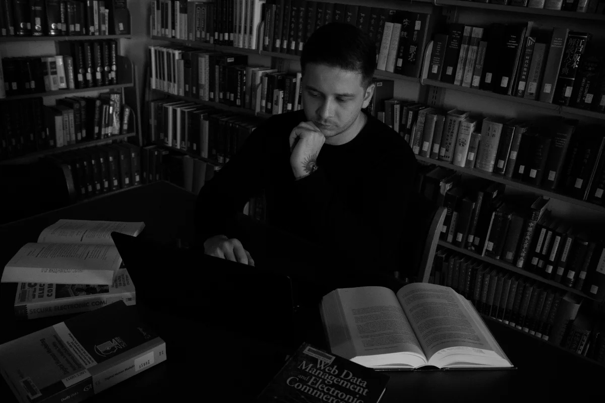 Vlad at a laptop in a library, surrounded by shelves of books